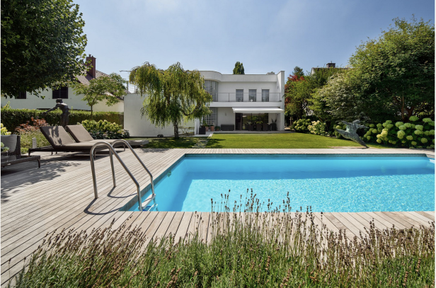 Modernes Haus mit Pool und Holzterrasse in einer sonnigen Umgebung.