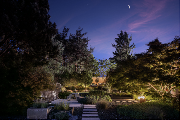 Stimmungsvoll beleuchteter Garten mit Sitzbereichen und Feuerschale unter Nachthimmel.