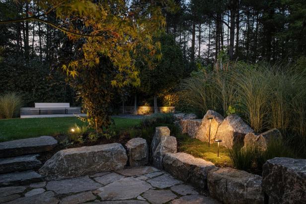 Ein Garten mit einem Steinweg und einer Bank, umgeben von üppigem Grün und bunten Blumen.
