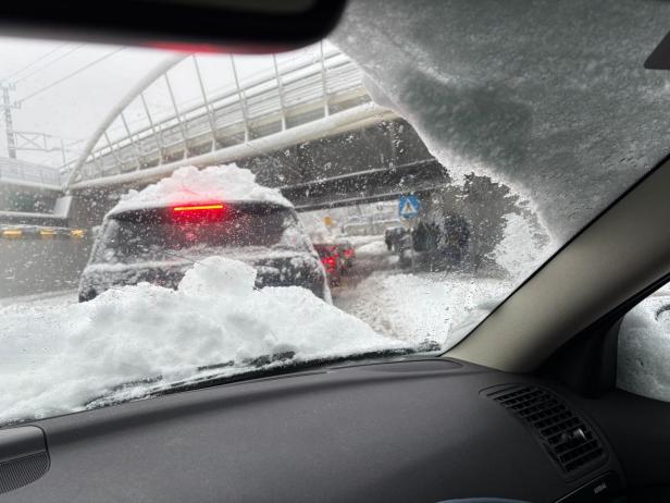 Vom Auto aus sieht man verschneite Autos im Stau unter einer Brücke.