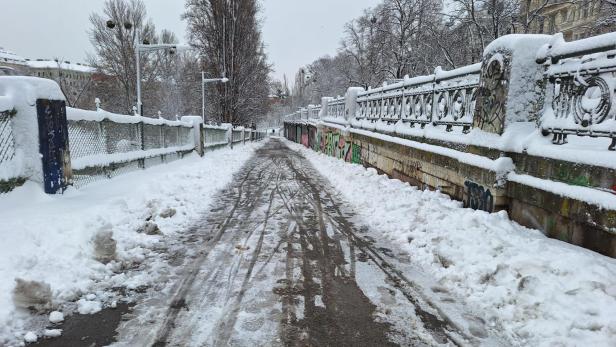 Ein verschneiter Weg mit Graffiti-Mauern und Bäumen im Hintergrund.