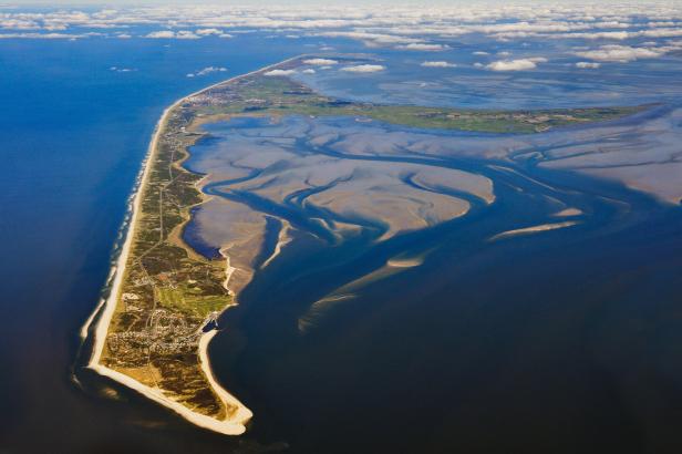 Sylt: Luftaufnahme einer langgestreckten Insel mit Sandstrand und Wattflächen im blauen Meer.