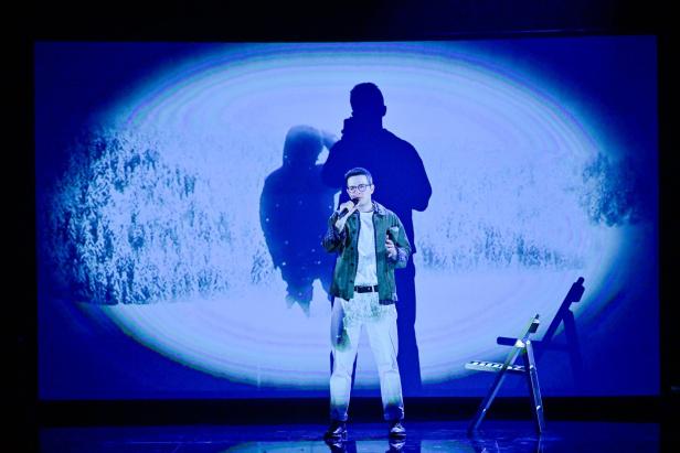 Ein Mann singt auf einer Bühne mit Mikrofon, im Hintergrund sind Schatten und eine winterliche Landschaft zu sehen.