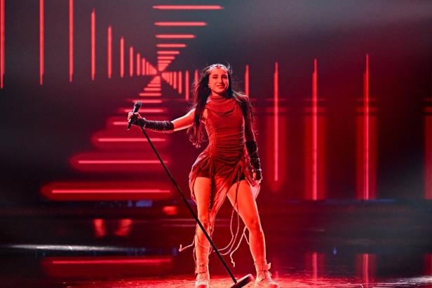 Eine Frau in rotem Outfit singt auf einer Bühne mit leuchtenden roten Lichteffekten im Hintergrund.