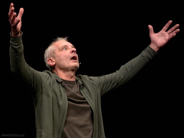 Ein Mann mit grauen Haaren hebt dramatisch beide Arme und blickt mit offenem Mund nach oben.