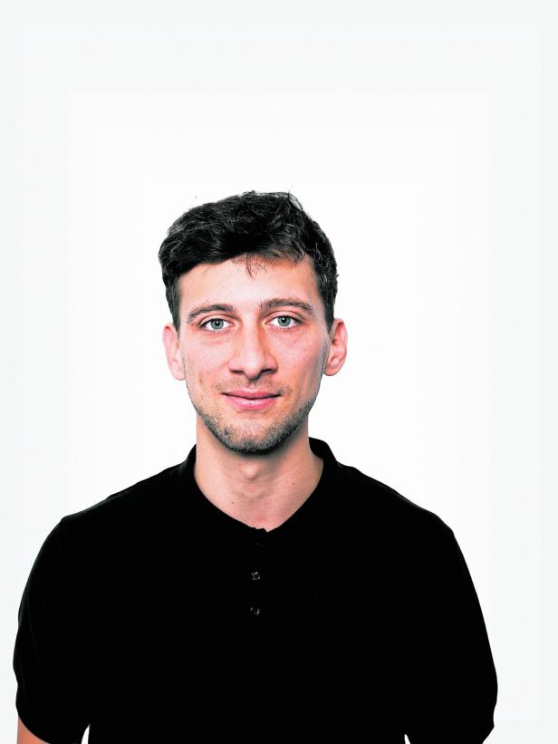 Junger Mann mit kurzen dunklen Haaren und schwarzem Hemd vor weißem Hintergrund.