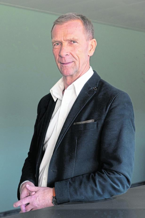 Ein Mann mit Jackett und Hemd steht vor einem hellgrünen Hintergrund.