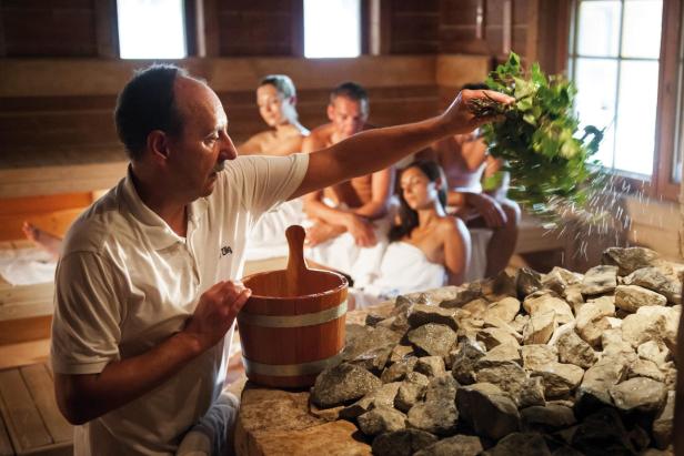 Saunameister führt einen Aufguss in einer fränkischen Wellness-Sauna durch, während Gäste entspannt auf Holzbänken sitzen.