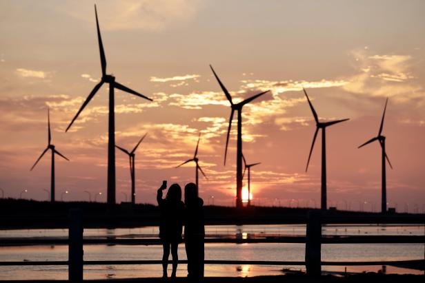 Zwei Menschen vor Windkraftanlagen im Sonnenuntergang.