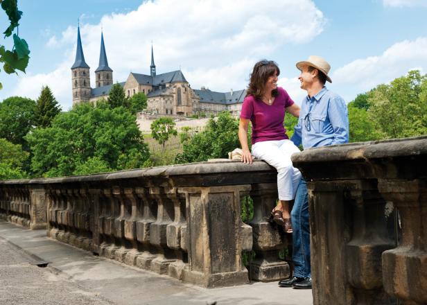 Ein Paar genießt den Ausblick auf das historische Kloster Michaelsberg in Bamberg, umgeben von grüner Natur und sommerlicher Atmosphäre.