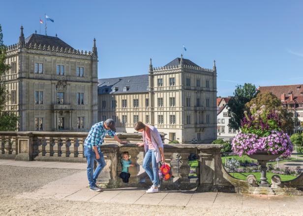 Eine Familie genießt einen sonnigen Tag im Hofgarten vor der historischen Residenz in Coburg, umgeben von Blumen und barocker Architektur.