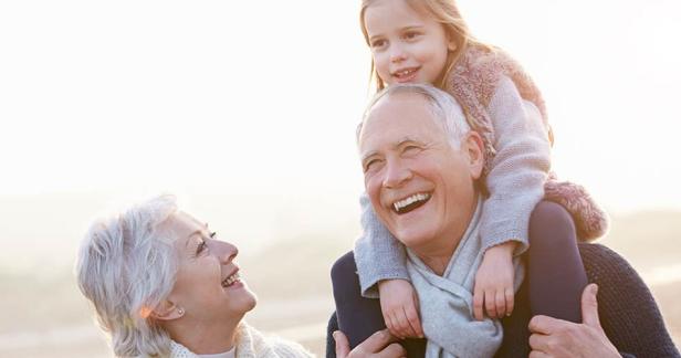 Älteres Paar lacht mit einem Kind, das auf den Schultern des Mannes sitzt, im Freien.