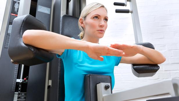 Frau trainiert an einer Kraftmaschine gezielt ihre Rückenmuskulatur in einem Fitnessstudio.