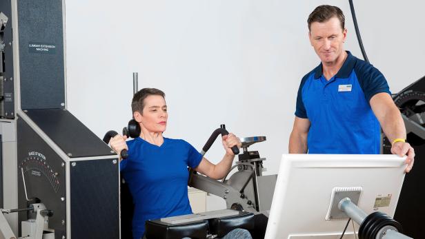 Ein Mann in blau hilft einer Frau in blau beim Training 