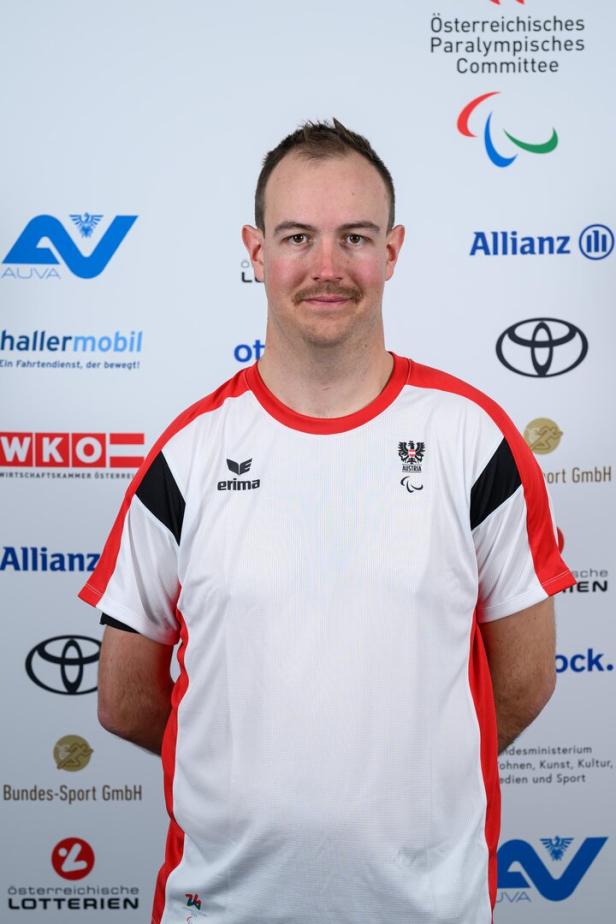 Manuel Rachbauer trägt ein weißes T-Shirt mit österreichischem Logo vor Sponsorenlogos.