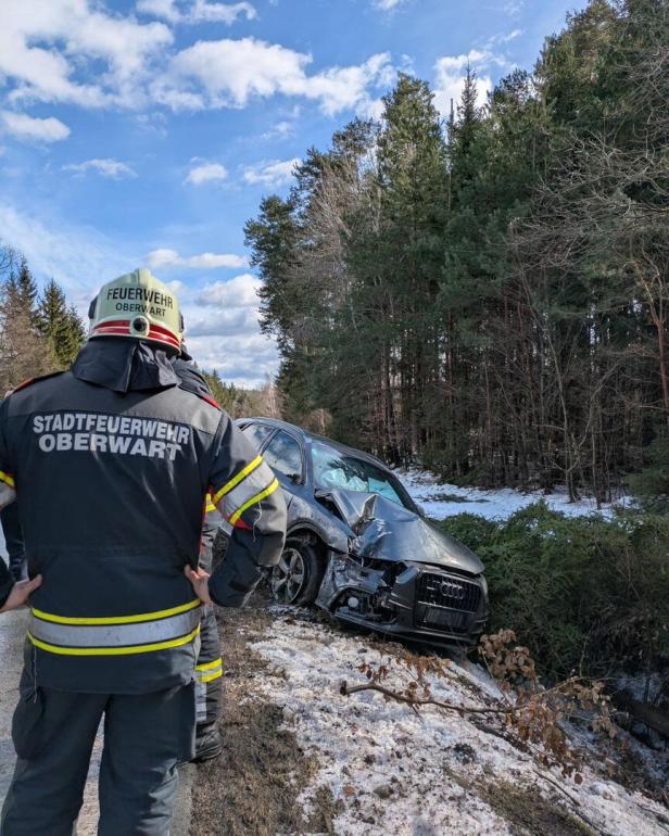 Ein Feuerwehrmann steht vor einem verunfallten Auto, das am Waldrand im Schnee liegt.