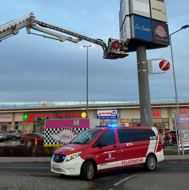 Ein Feuerwehrfahrzeug und eine Drehleiter mit Feuerwehrleuten im Einsatz an einer großen Werbetafel vor Geschäften.