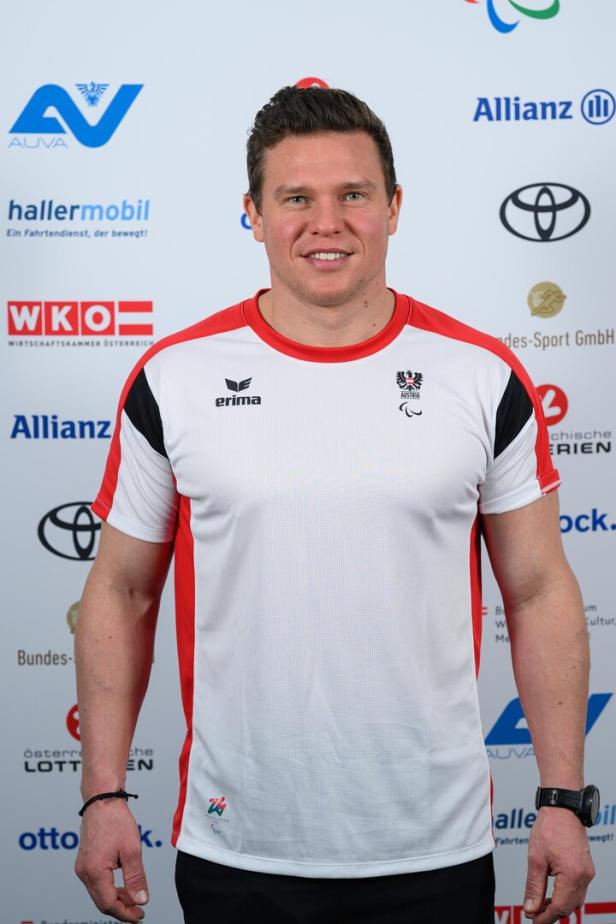 Stefan Winter trägt ein weißes Sportshirt mit roten Akzenten und steht vor einer Sponsorenwand.