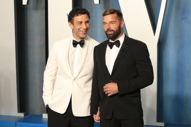 Jwan Yosef und Ricky Martin posieren gemeinsam in eleganten Smokings vor einer blauen Wand.