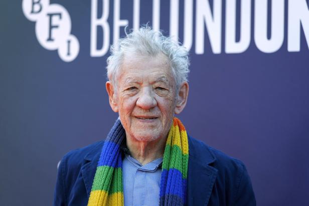 Ian McKellen lächelt vor einem BFI London Film Festival-Hintergrund und trägt einen bunten Regenbogen-Schal.