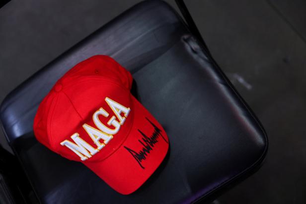 Auf einem schwarzen Stuhl liegt eine rote "MAGA"-Kappe mit einer Unterschrift.