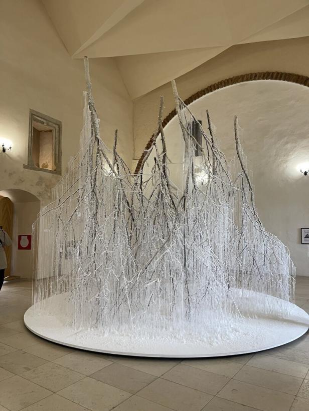 Im Raum steht eine Installation aus Ästen, die mit weißen Fäden wie Eiszapfen behangen sind.