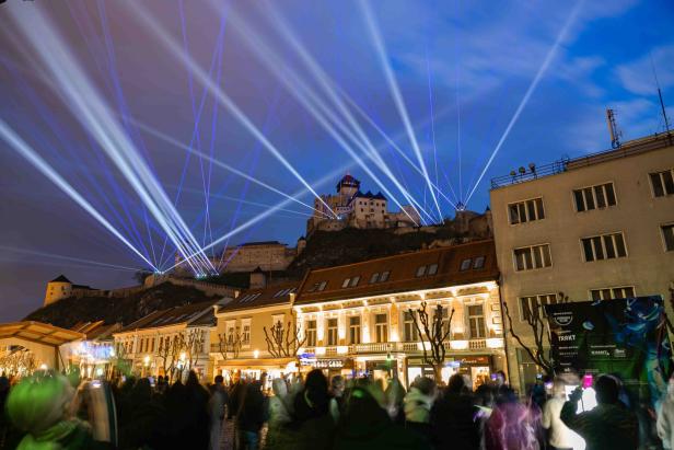 Eine Menschenmenge blickt auf die Burg, die von blauen Lichtstrahlen erhellt wird.