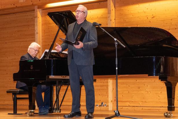 Ein Mann singt mit Notenmappe vor einem Mikrofon, während ein anderer Mann am Flügel Klavier spielt.