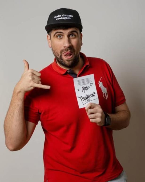Ein Mann mit Kappe und rotem Polohemd hält ein Schild und formt eine Telefon-Geste.