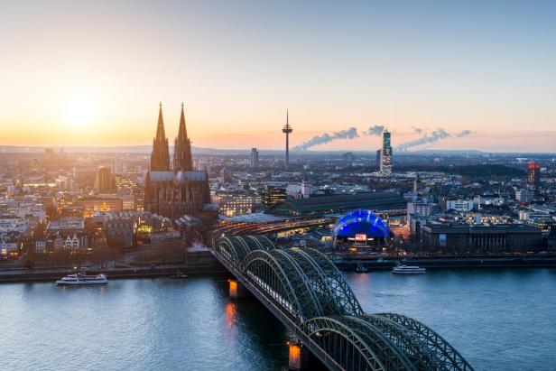 Kranhäuser und Kölner Dom am Rhein bei Sonnenuntergang, beleuchtete Skyline.