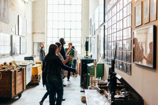 Besucher betrachten eine Ausstellung mit Fotos und historischen Objekten in einem hellen Raum.
