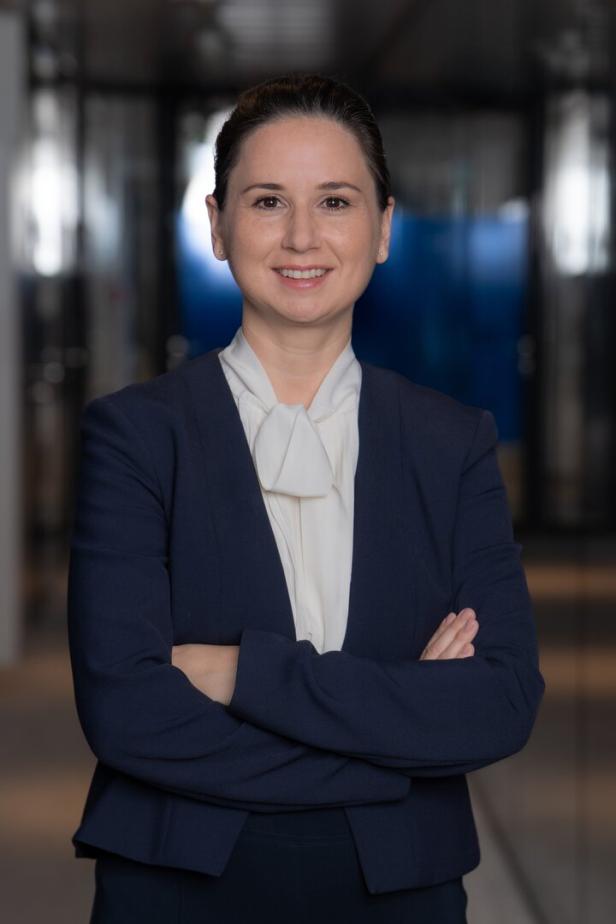 Eine Frau mit verschränkten Armen trägt ein blaues Jackett und eine weiße Bluse.