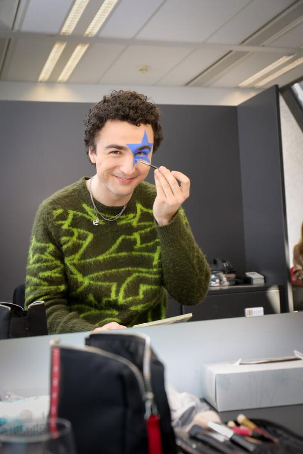 Eine Person malt sich mit einem Pinsel einen blauen Stern um das rechte Auge ins Gesicht.