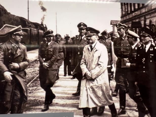Mehrere Männer,darunter Adolf Hitler,  in Uniformen gehen gemeinsam auf einem Bahnsteig neben einem Zug.