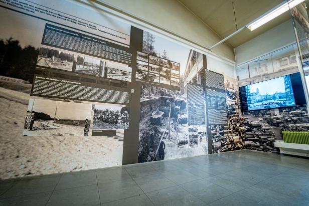 Eine Ausstellung mit historischen Fotos, Texttafeln und einem Bildschirm zeigt Informationen zur Panzerproduktion im Zweiten Weltkrieg.