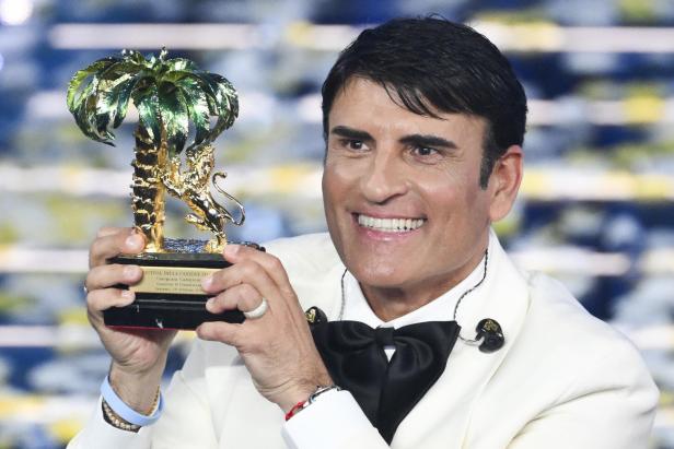 Ein lächelnder Sal de Vinci im weißen Anzug hält seine goldene Trophäe.