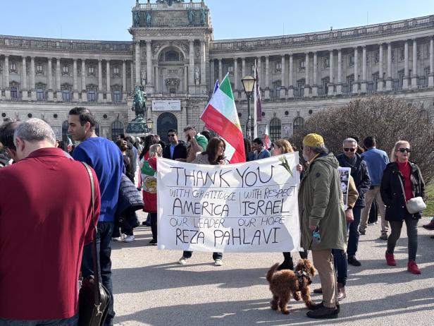 Mehrere Menschen versammeln sich vor einem historischen Gebäude, halten eine große Dankesbotschaft und schwenken Fahnen.