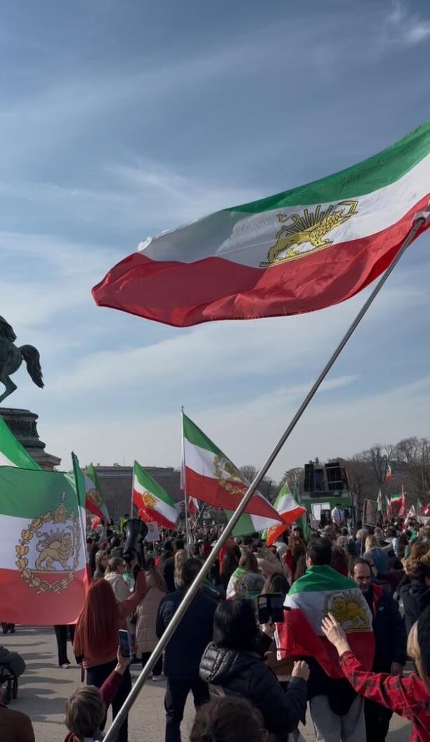 Viele Menschen versammeln sich im Freien und schwenken grün-weiß-rote Fahnen mit einem goldenen Löwenemblem.