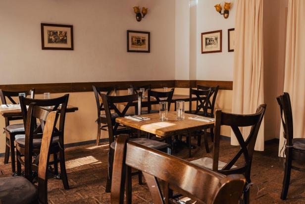 Mehrere gedeckte Holztische mit dunklen Stühlen in einem gemütlichen, leeren Restaurant mit Wandbildern und warmem Licht.