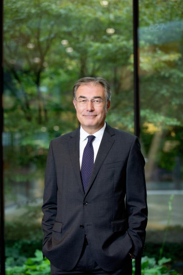 Ein Mann mit Brille und Anzug steht vor einem Fenster mit Blick ins Grüne.