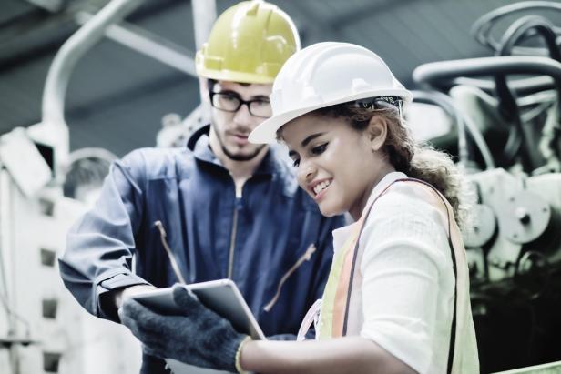 Zwei Fachkräfte mit Schutzhelmen besprechen auf einer Baustelle mithilfe eines Tablets technische Details zur frühzeitigen Einbindung von Facility Management.