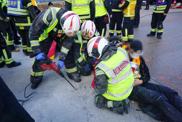 Mehrere Feuerwehrleute befreien eine Person mit schwerem Gerät aus einer misslichen Lage auf der Straße.