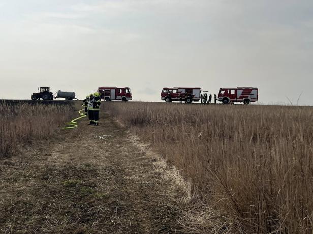 Mehrere Feuerwehrleute und drei Einsatzfahrzeuge stehen auf einem Feldweg neben einem Traktor mit Wassertank.