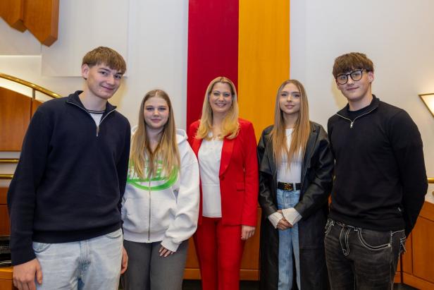 Fünf Personen stehen nebeneinander in einem Raum mit Holzverkleidung und einer rot-gelben Wanddekoration.