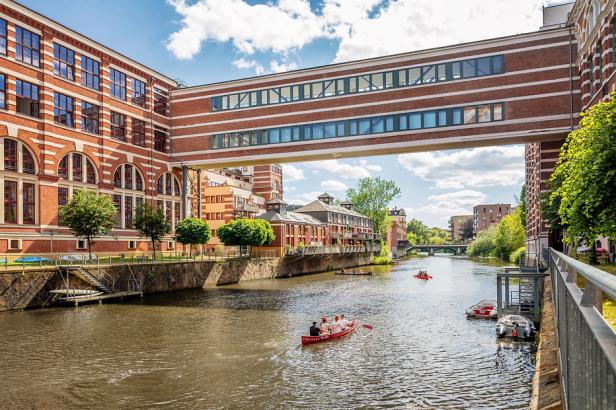 Menschen fahren mit Booten auf dem Karl-Heine-Kanal entlang der historischen Backsteinbauten der Buntgarnwerke in Leipzig.