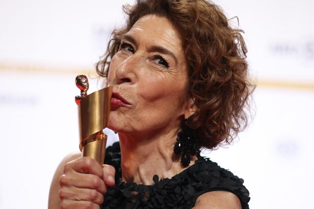 Adele Neuhauser mit lockigem Haar küsst eine goldene Trophäe.