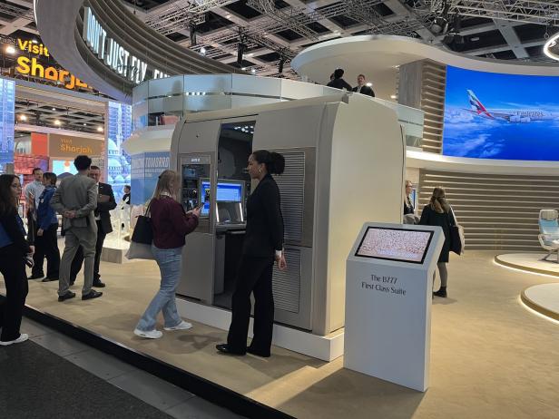 Mehrere Menschen stehen an einem Messestand, an dem eine Emirates First Class Suite des B777 ausgestellt ist.