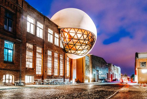 Niemeyer Sphere, eine große weiße Kugel mit einer geometrischen Glasstruktur ragt aus der Seite eines Backsteingebäudes in der Nähe der Baumwollspinnerei in Leipzig