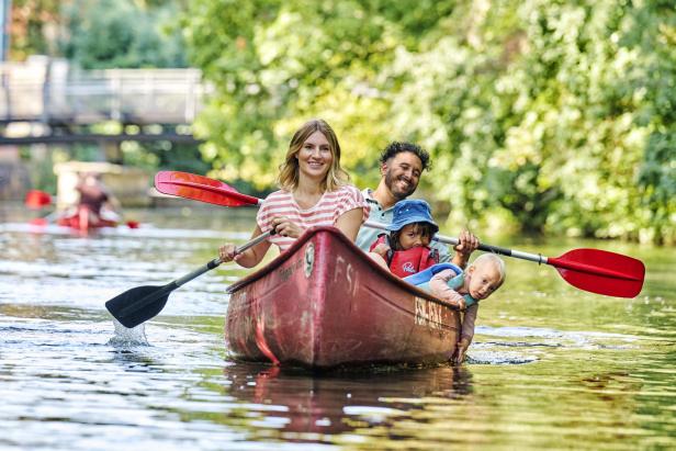 Eine Familie fährt bei sommerlichen Wetter mit einem roten Kanu auf den Wasserwegen in Leipzig.