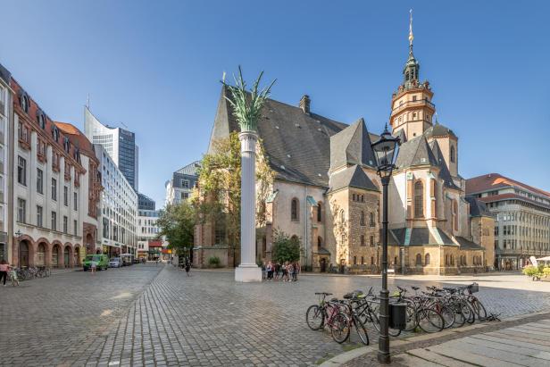 In Leipzig ist die Nikolaikirche von der Seite zu sehen. Das Gebäude ist aus Stein mit einem hohen, spitzen Dach und vielen Fenstern.